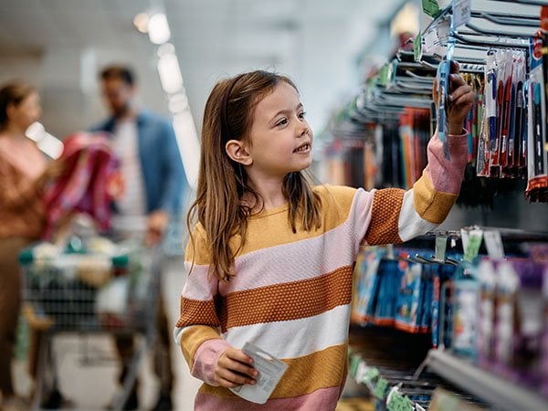 Young girl in a striped shirt shopping for items on shelves.