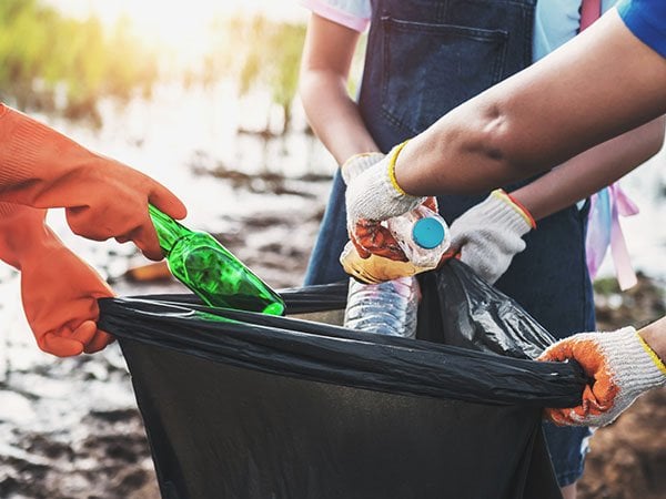 Volunteers wearing gloves placing plastic bottles into a black trash bag